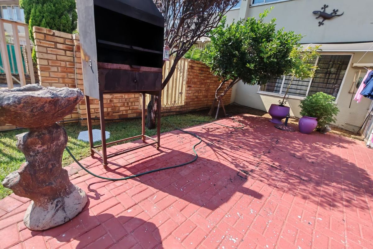 A private rear courtyard featuring red paved flooring, a built-in brick boundary wall, and a metal braai area.