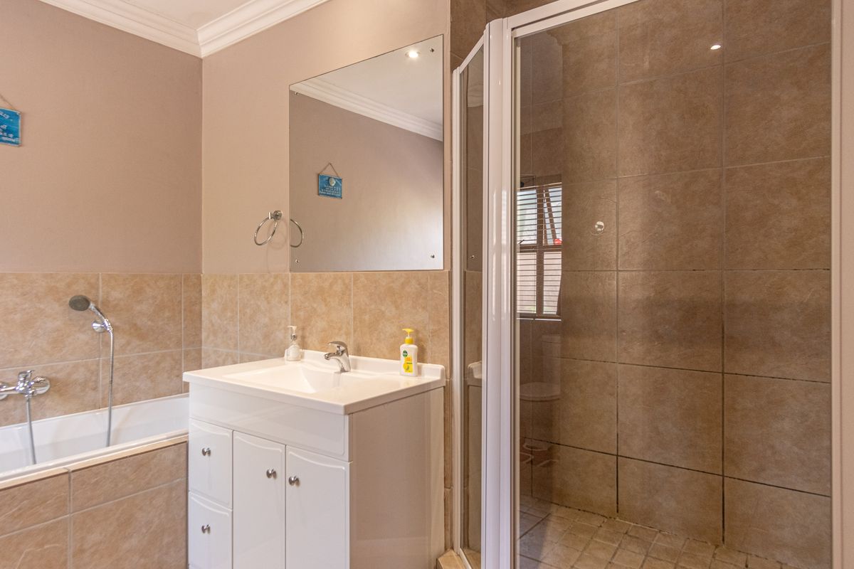 A functional bathroom featuring a tiled bathtub, a separate shower enclosure with a glass door, and a vanity basin with a wall-mounted mirror.