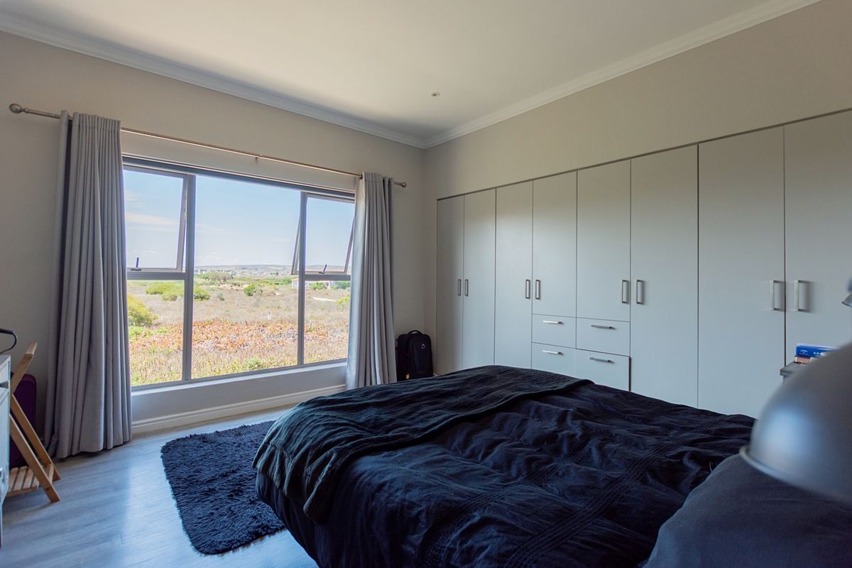 A well-maintained bedroom featuring extensive built-in cupboards, modern laminate flooring, and large windows offering scenic landscape views.