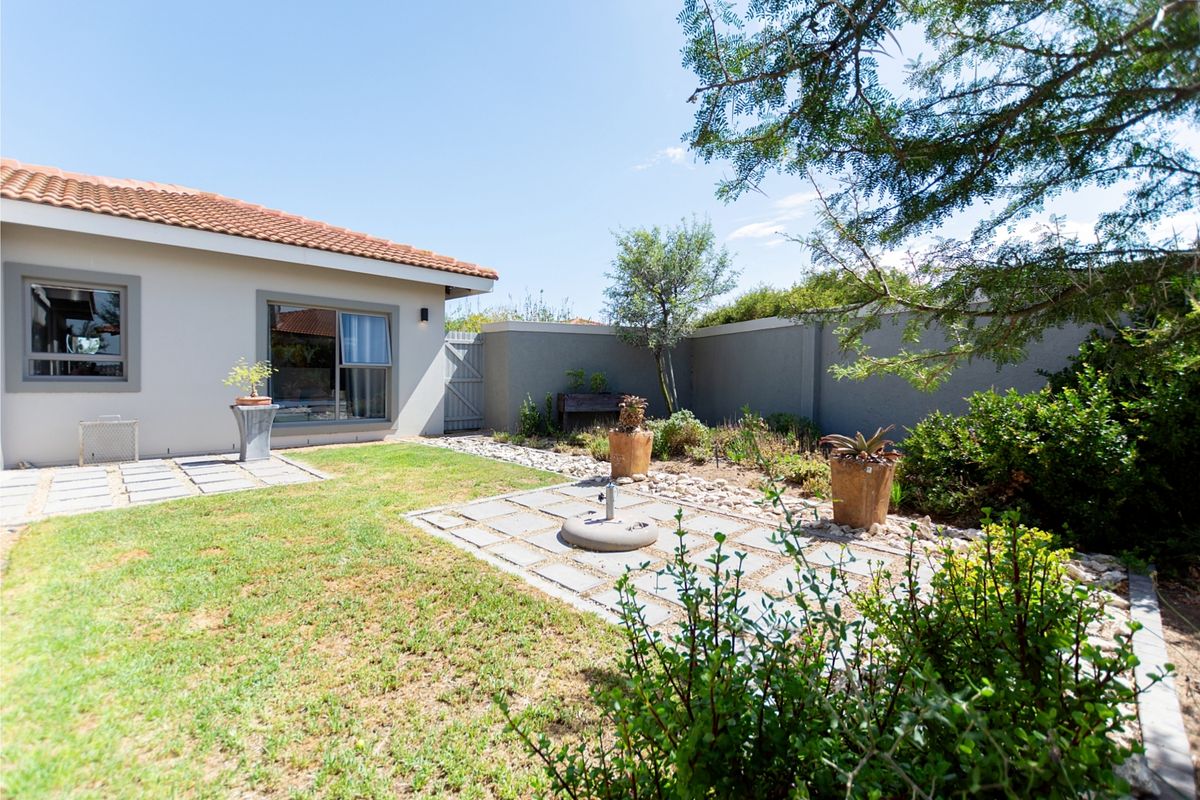 A well-maintained rear garden featuring a paved patio area, established landscaping, and a secure boundary wall, providing a private outdoor space.