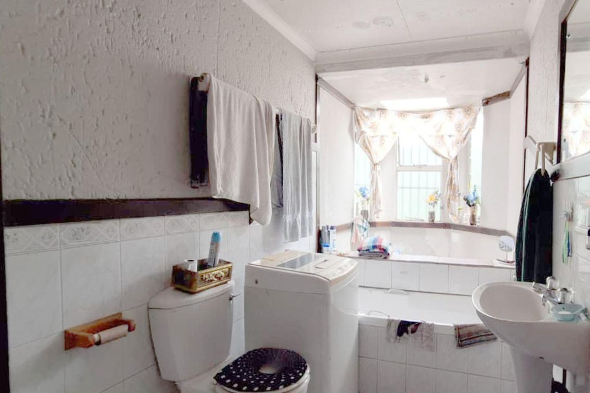 A functional bathroom featuring a built-in bathtub, pedestal basin, and toilet, with integrated laundry space and natural light from a window.