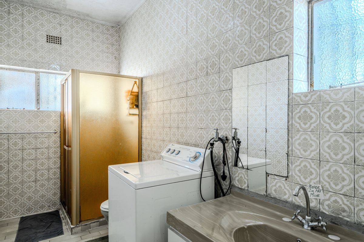 A dated bathroom featuring full-height patterned wall tiles, a shower enclosure, and a built-in vanity basin with plumbing fixtures.