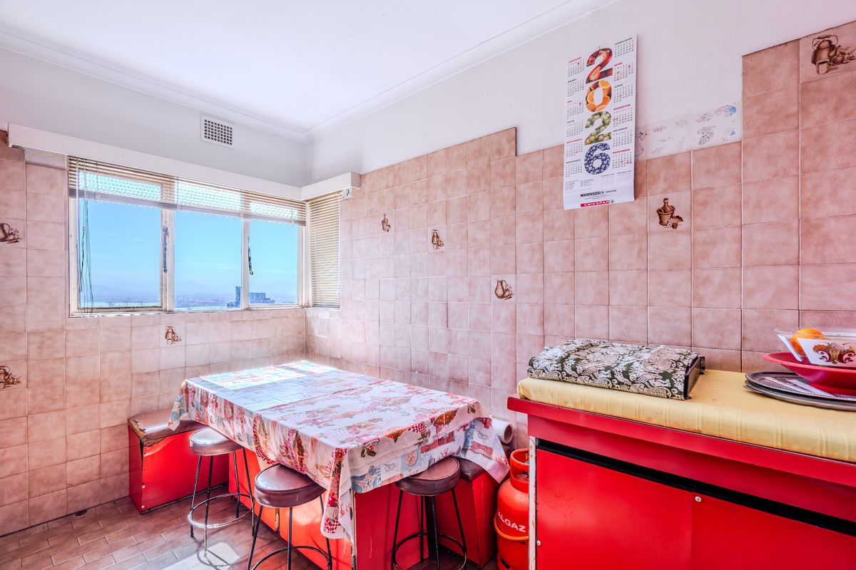 A dated kitchen area featuring full-height wall tiling, tiled flooring, and a window with natural light, offering potential for a modern renovation.