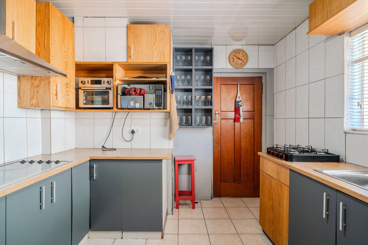 A functional kitchen featuring a mix of grey and timber cabinetry, gas hob, extractor fan, and tiled finishes throughout.