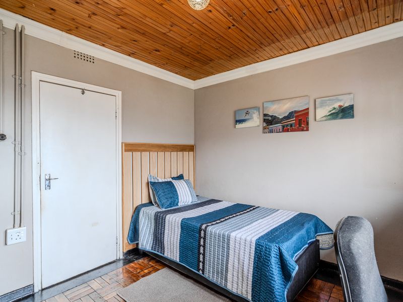 A bedroom featuring parquet flooring, a timber-clad ceiling, and a built-in headboard, with neutral wall finishes.