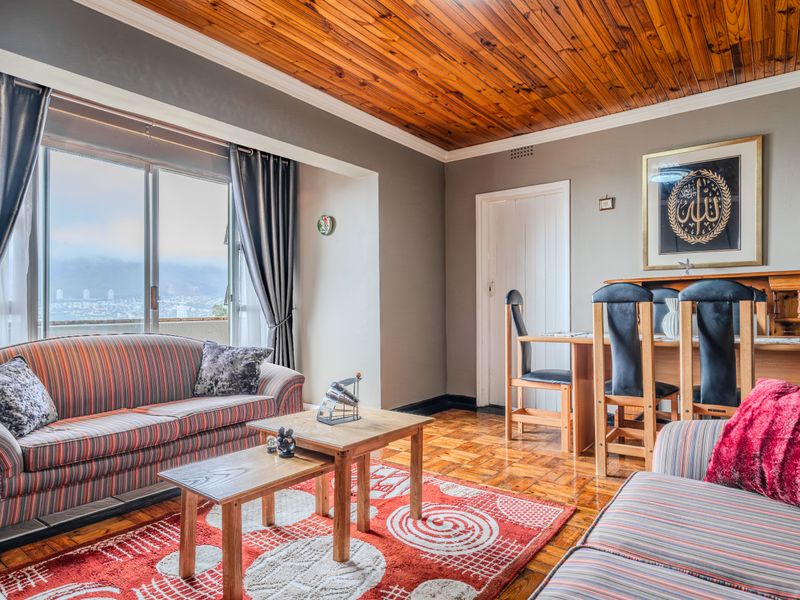 Open-plan living and dining area featuring warm timber tongue and groove ceilings, classic parquet flooring, and large sliding doors with expansive city views.