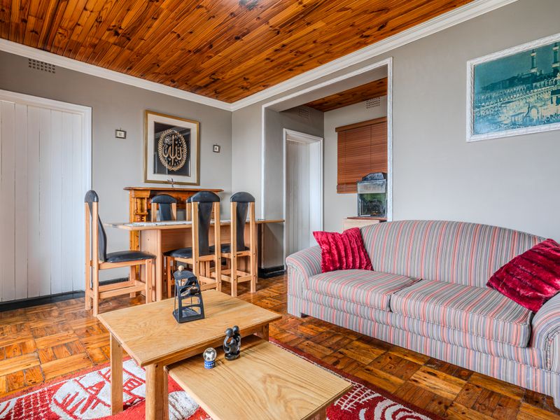 Open plan living and dining area featuring warm parquet flooring, a timber-clad ceiling, and a classic fireplace mantel.