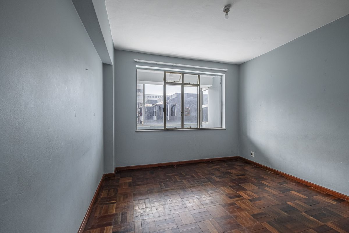An empty bedroom featuring classic parquet flooring and a large metal-framed window, offering a blank canvas for potential interior design updates.