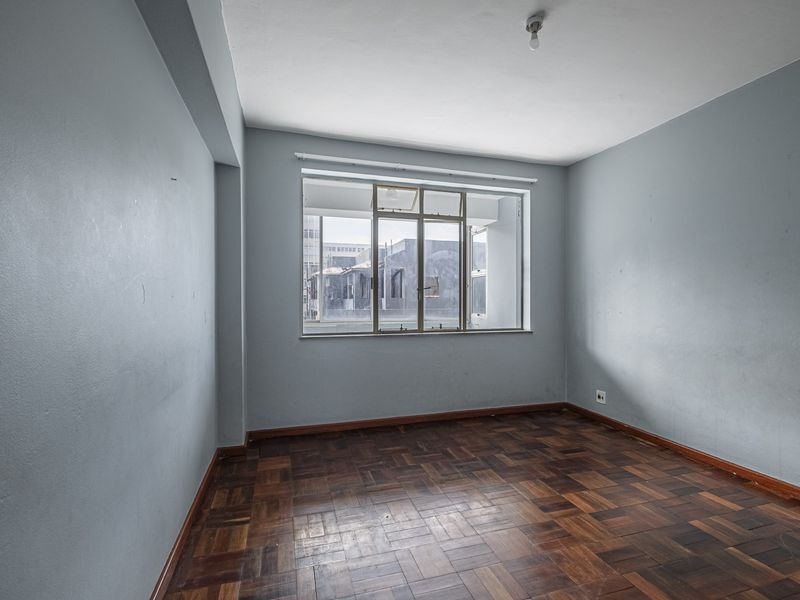 An empty bedroom featuring classic parquet flooring and a large metal-framed window, offering a blank canvas for potential interior design updates.