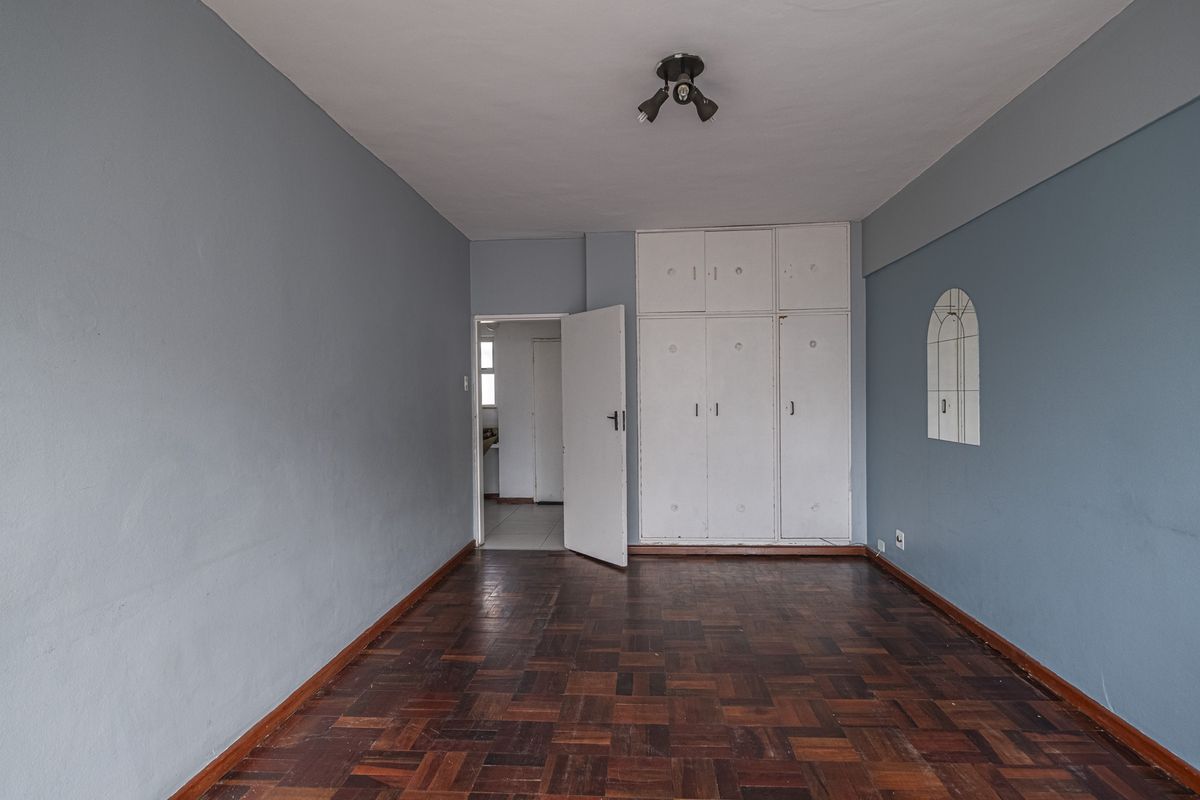 An empty bedroom featuring original parquet flooring, built-in cupboards, and a neutral blue wall finish, offering a blank canvas for renovation.