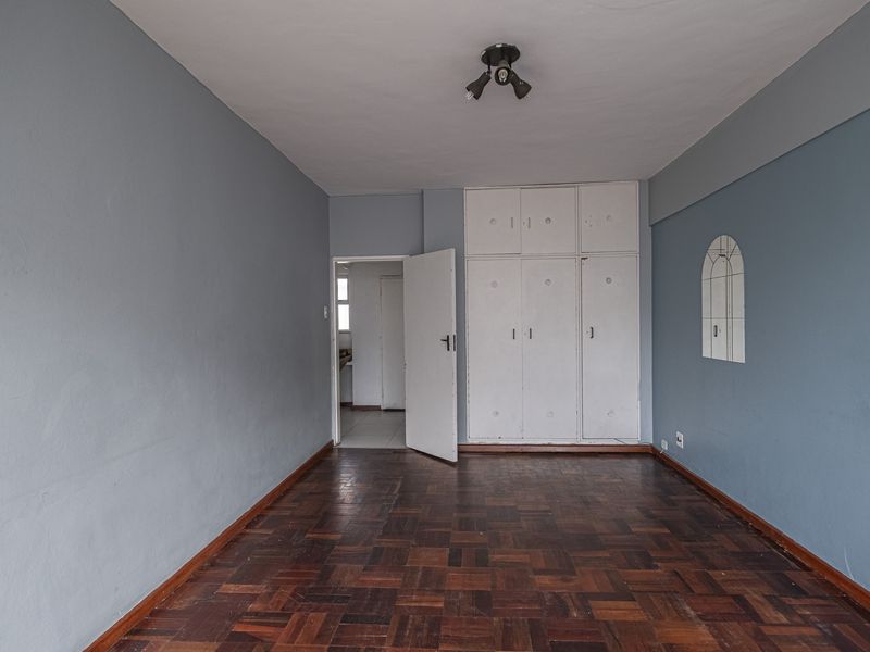 An empty bedroom featuring original parquet flooring, built-in cupboards, and a neutral blue wall finish, offering a blank canvas for renovation.