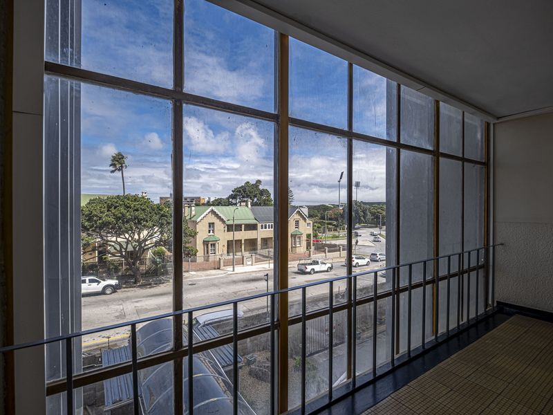 An enclosed balcony or walkway featuring large metal-framed windows with views over the street and surrounding neighborhood.