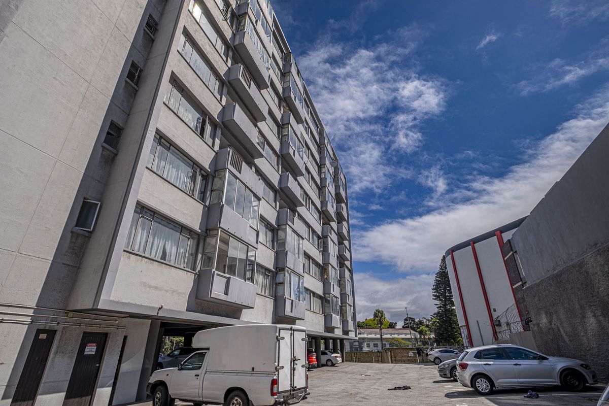 Exterior view of the apartment building showing the rear facade, enclosed balconies, and the associated paved parking area.
