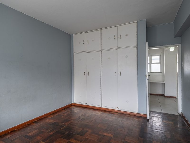 A vacant bedroom featuring original parquet flooring and floor-to-ceiling built-in cupboards, offering a neutral canvas for potential updates.