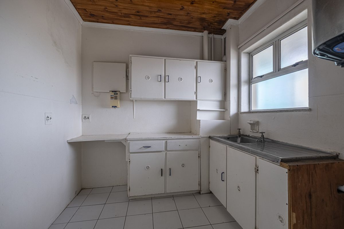A dated kitchen featuring original built-in cabinetry, a stainless steel sink, tiled flooring, and a timber ceiling, offering significant potential for renovation.