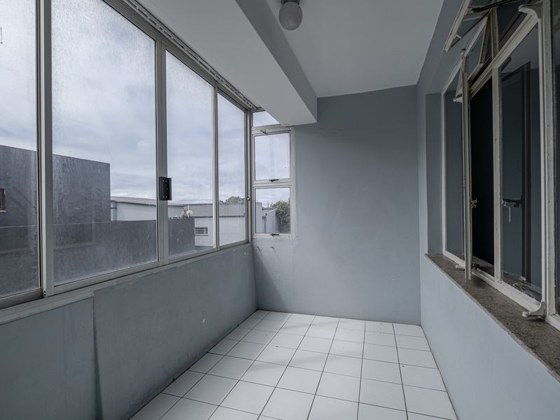 An enclosed balcony featuring tiled flooring and large aluminium-framed windows, offering a versatile space that could be used as a sunroom or study area.