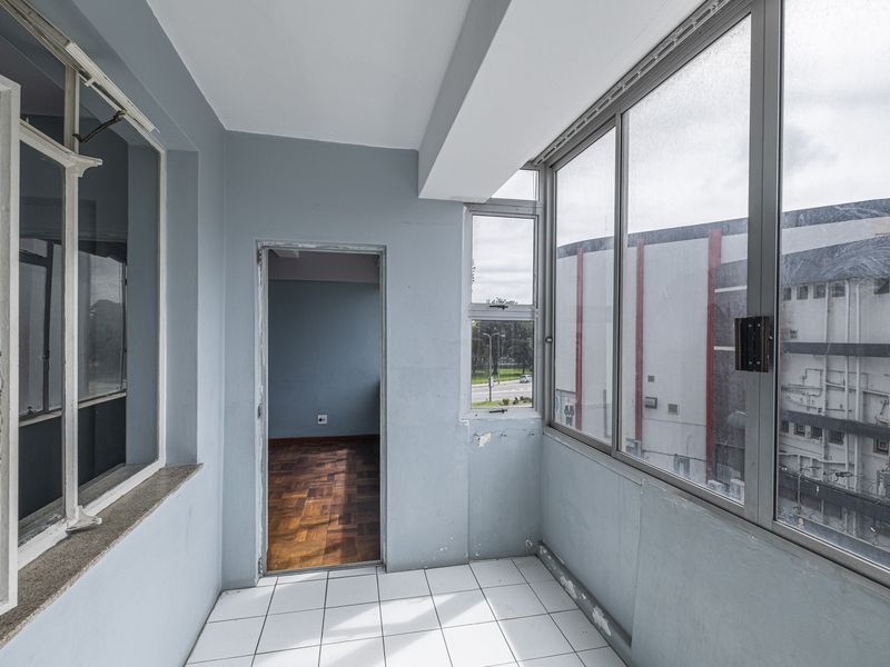An enclosed balcony featuring tiled flooring and aluminium window frames, offering a view of the surrounding urban area.