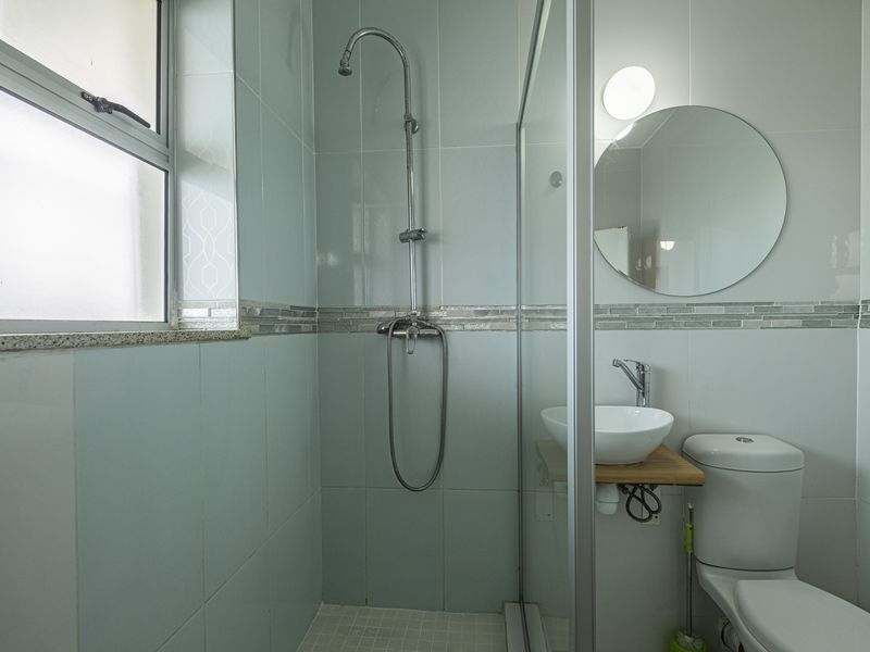 A clean, modern bathroom featuring a glass-enclosed shower, a vessel basin on a wooden shelf, and a toilet, finished with light blue wall tiles.