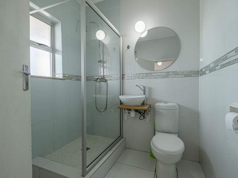 A compact, modern bathroom featuring a glass-enclosed shower, a vessel sink on a wooden shelf, and a white toilet with tiled finishes.