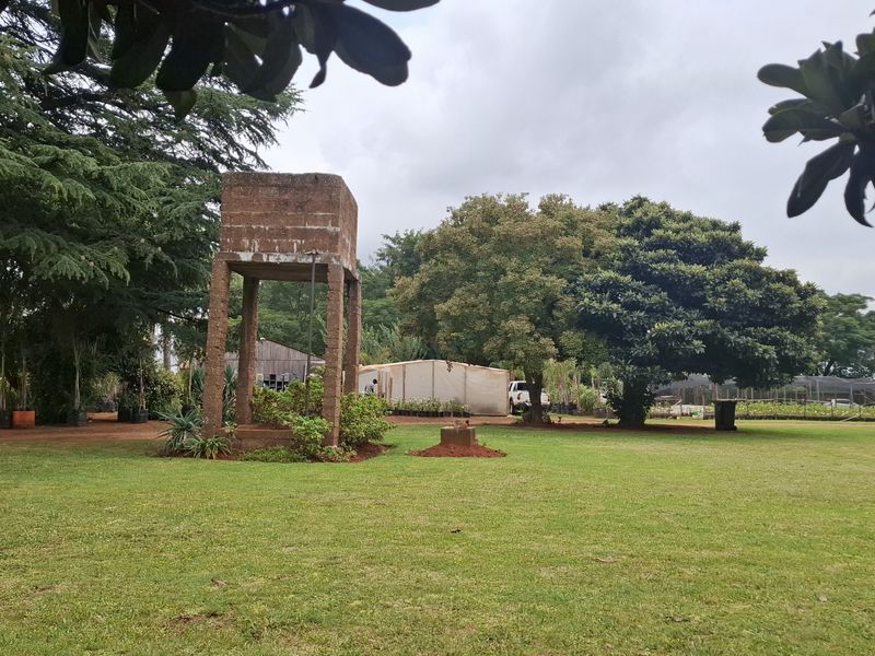 Expansive garden area featuring a prominent brick water tower, mature trees, and established nursery infrastructure on the small holding property.
