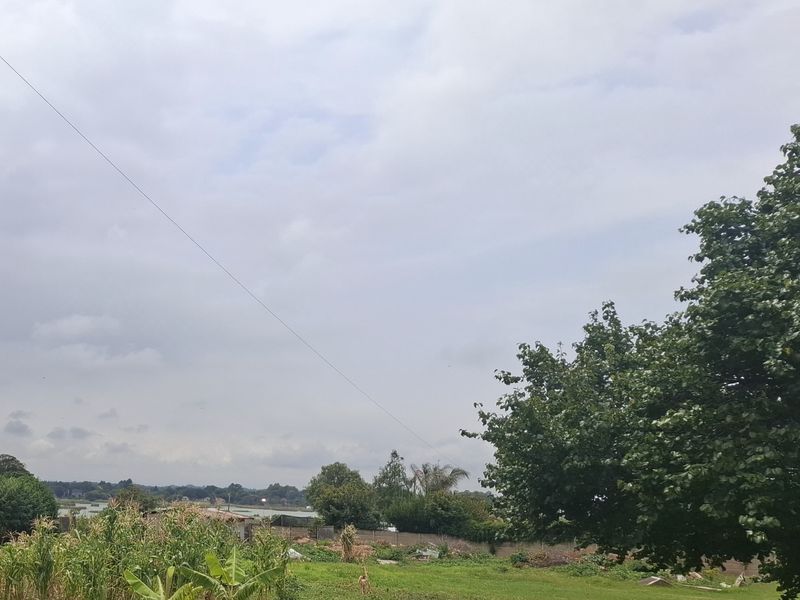 A scenic view of the property grounds featuring mature trees, open green space, and a perimeter wall under a cloudy sky.