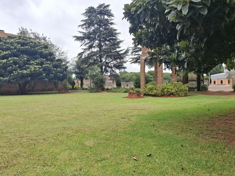 A spacious, well-maintained garden area featuring mature trees, established lawn, and brick pillar entrance details on a small holding property.