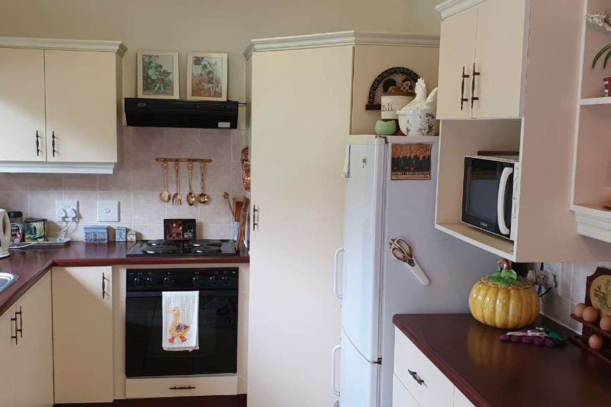 A functional kitchen featuring cream-colored cabinetry, laminate countertops, a built-in oven with hob, and a stainless steel double sink with tiled backsplash.