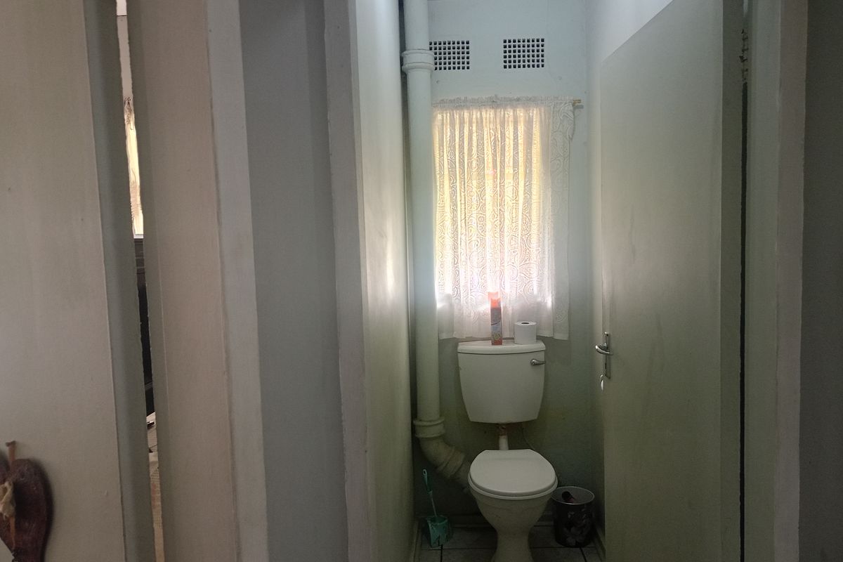 A compact bathroom featuring a standard toilet, tiled flooring, and an exposed vertical plumbing pipe.