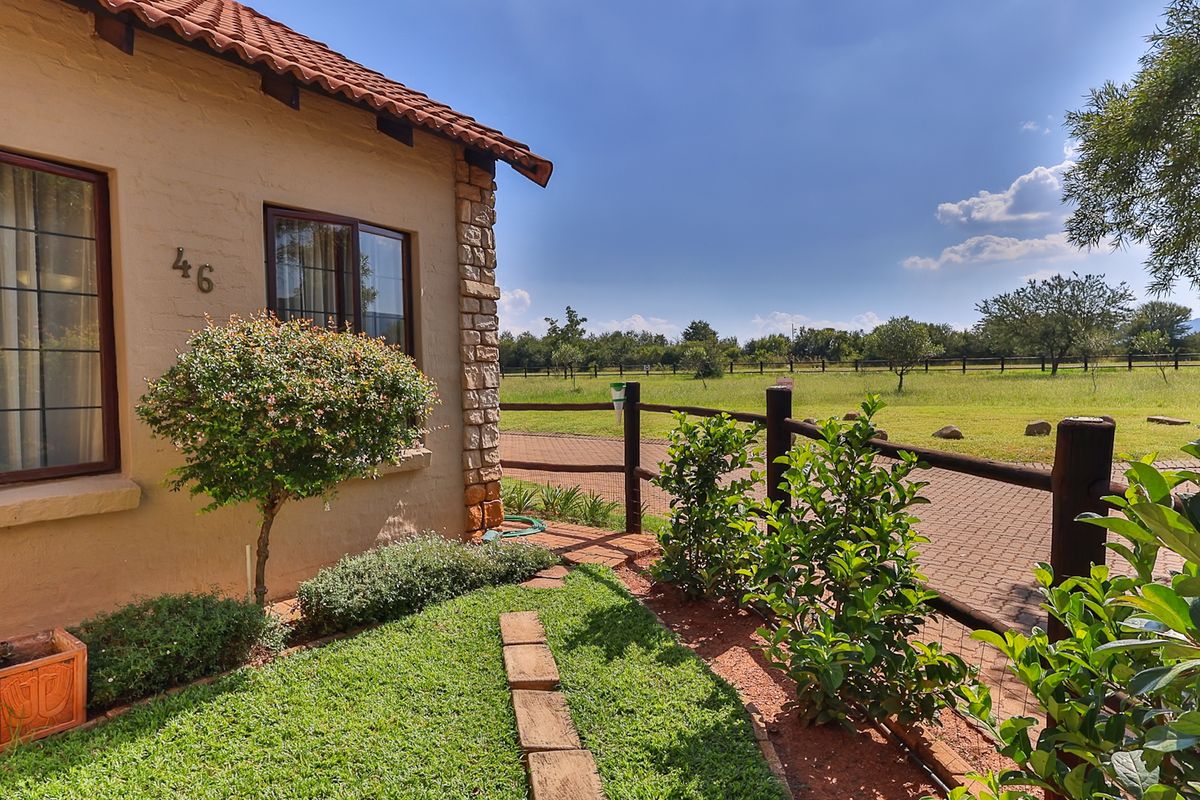 A well-maintained townhouse exterior featuring stone cladding, terracotta roof tiles, and a private garden overlooking an open field with post and rail fencing.