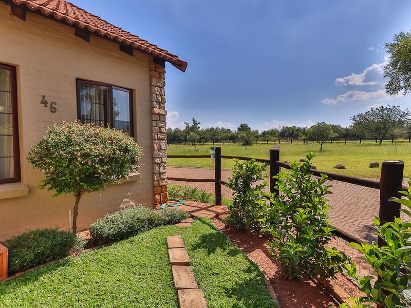 A well-maintained townhouse exterior featuring stone cladding, terracotta roof tiles, and a private garden overlooking an open field with post and rail fencing.