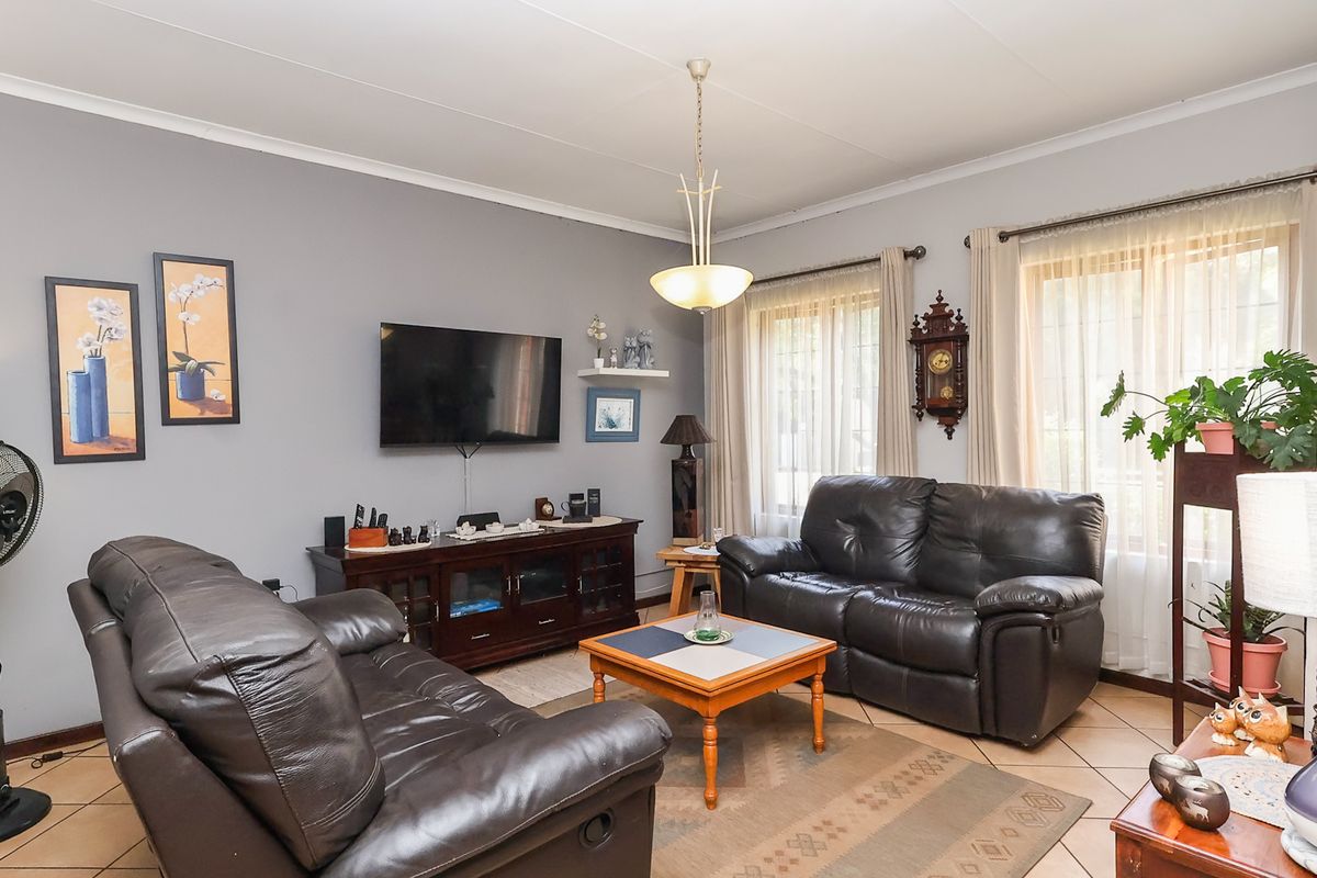 A comfortable living room featuring tiled flooring, neutral grey walls, and large windows with natural light, providing a functional and inviting space.