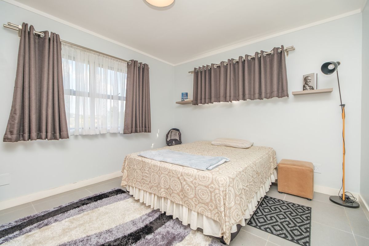 A bedroom featuring tiled flooring, neutral wall paint, and wall-mounted shelving units, providing a functional and well-lit sleeping space.