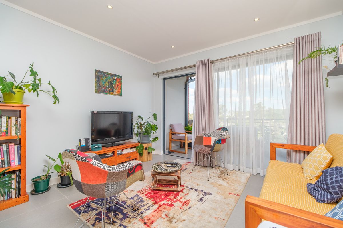 A bright living room featuring tiled flooring, recessed downlighting, and a large sliding glass door providing direct access to the balcony.
