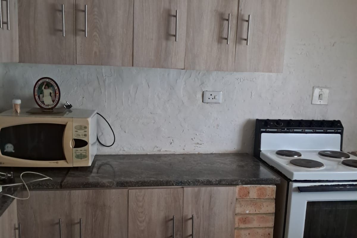A functional kitchen featuring light wood-look cabinetry, stone-effect countertops, and a freestanding electric stove with unique exposed brick detailing.