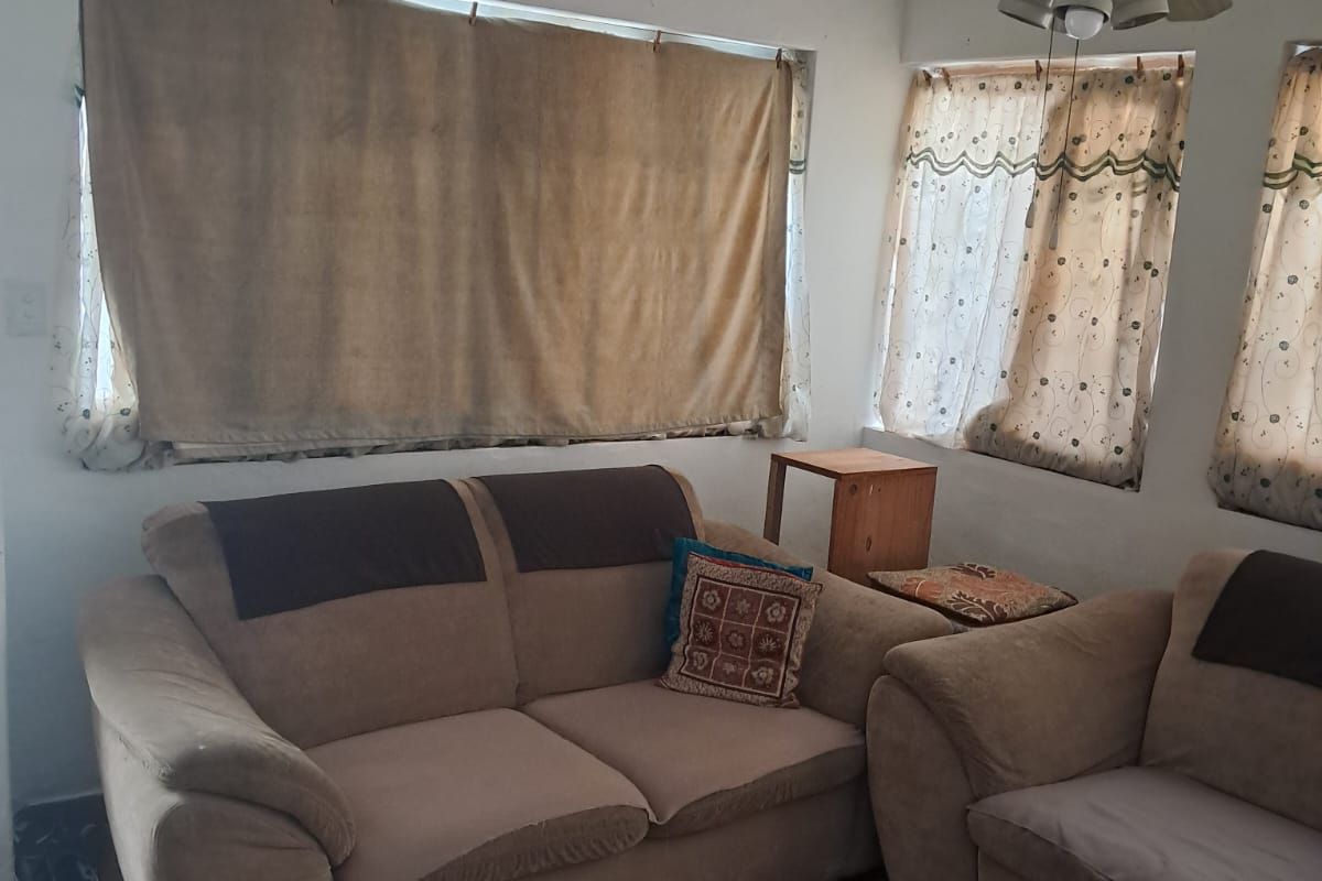 A living room area featuring ceramic floor tiles and a ceiling fan, with multiple windows providing natural light.