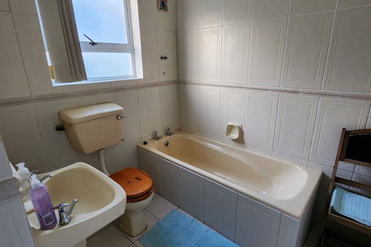 A dated bathroom featuring a cream-colored bathtub, pedestal basin, and toilet, finished with wall tiles and a window for natural light.