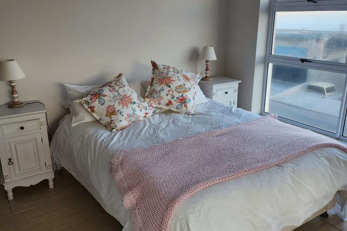 A bright bedroom featuring large windows with coastal views and neutral tiled flooring.