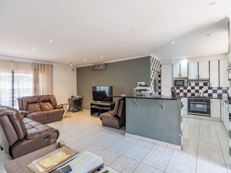 Open-plan living and kitchen area featuring tiled floors, modern cabinetry, built-in appliances, and a breakfast bar, creating a functional and connected living space.