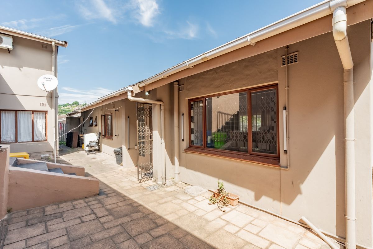 A paved rear exterior area featuring security gates, guttering, and downpipes, providing access to the side of the property.