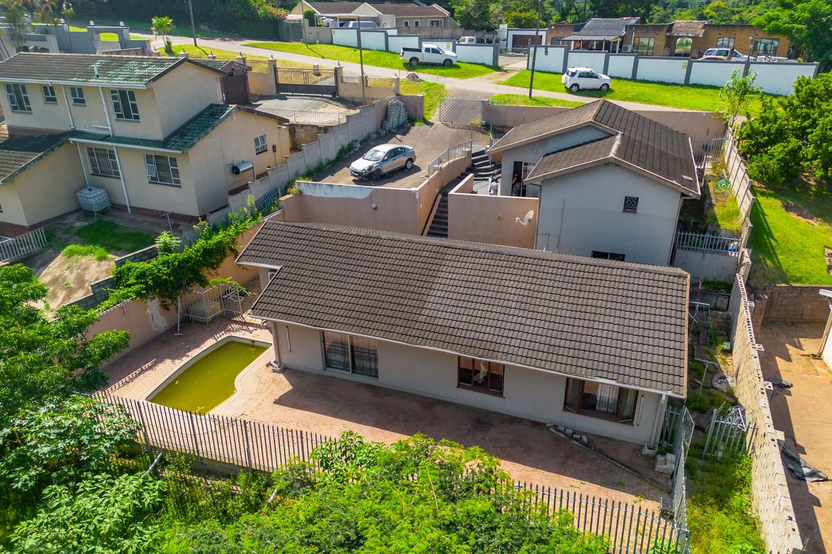 Aerial view of the property showing the main dwelling, paved patio area, swimming pool, and surrounding perimeter fencing.