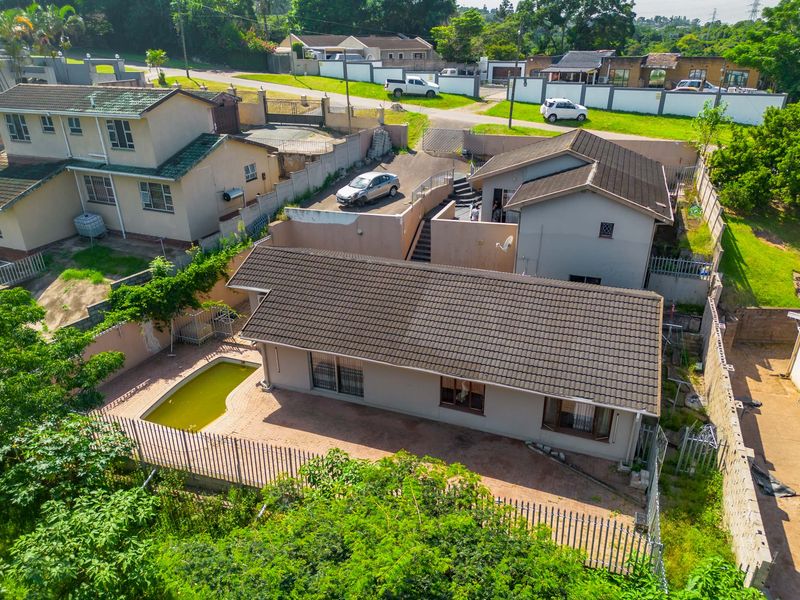 Aerial view of the property showing the main dwelling, paved patio area, swimming pool, and surrounding perimeter fencing.