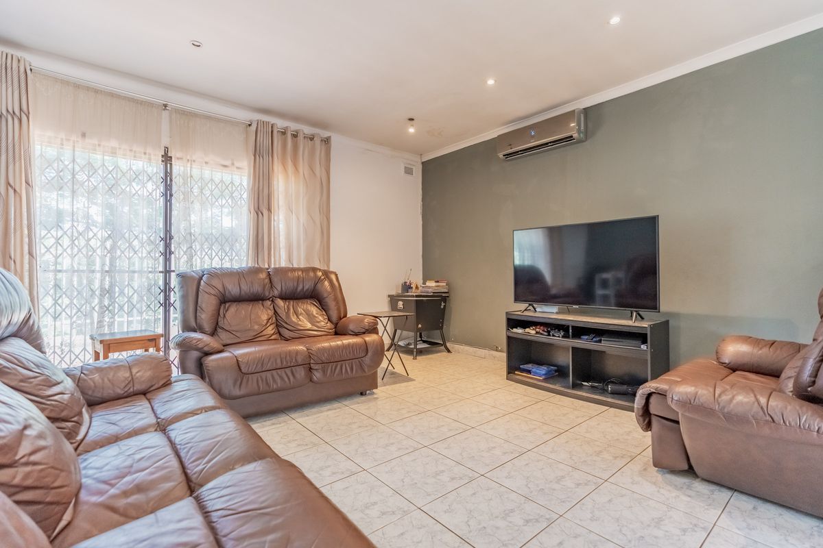 A comfortable living room featuring tiled flooring, a wall-mounted air conditioning unit, and sliding glass doors with security gates leading to the exterior.