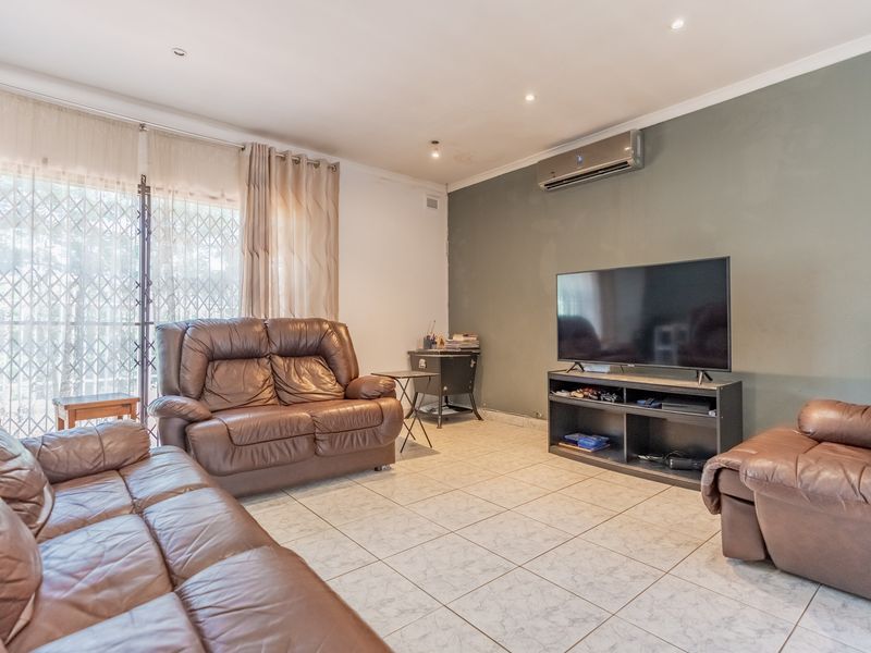 A comfortable living room featuring tiled flooring, a wall-mounted air conditioning unit, and sliding glass doors with security gates leading to the exterior.