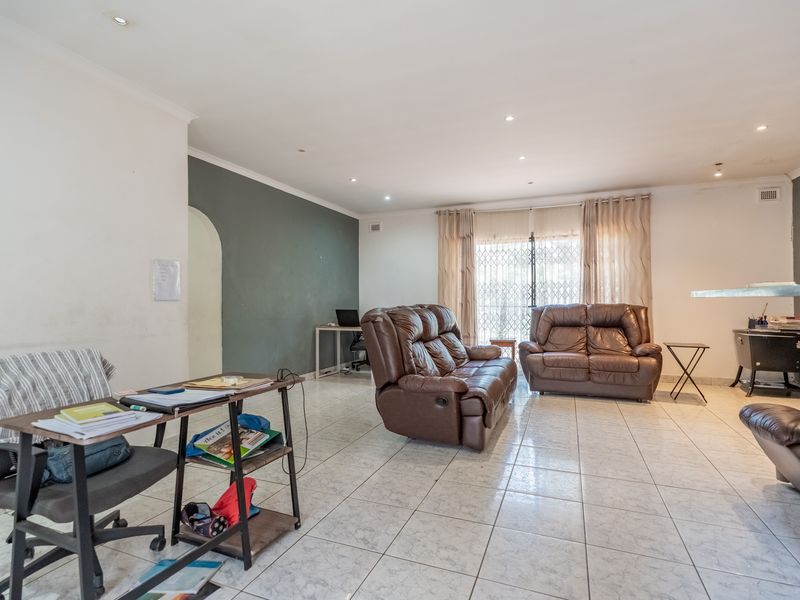 Spacious living room featuring tiled flooring, recessed downlighting, and a sliding door with security gate leading to the exterior.