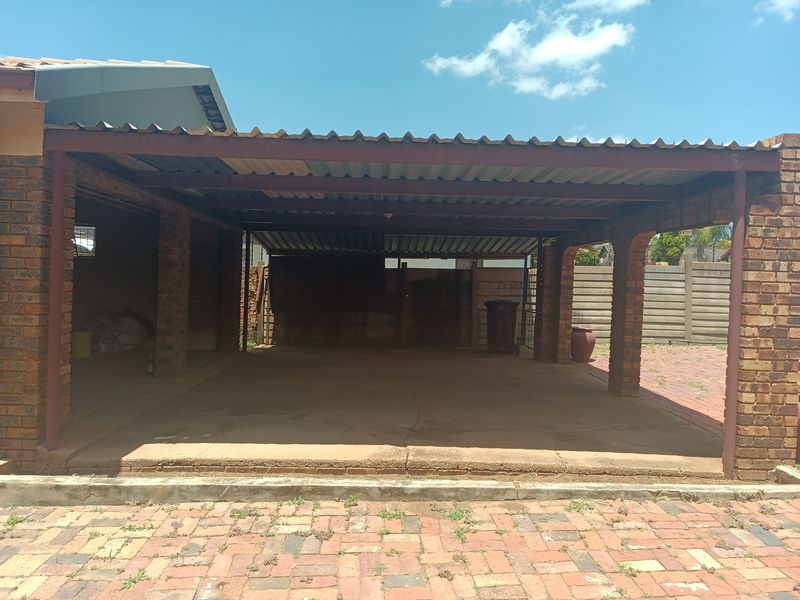 An open-sided brick garage structure with a corrugated metal roof and concrete flooring, situated on a paved driveway.