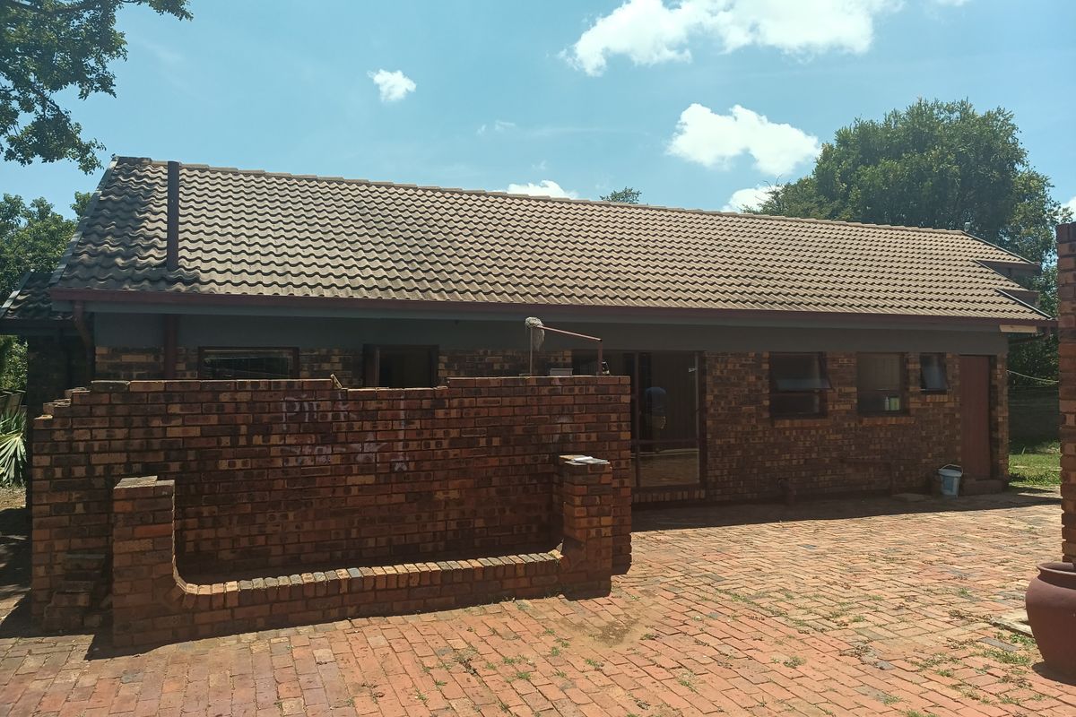 Rear view of a face brick house featuring a tiled roof, brick paved patio area, and a low brick boundary wall.
