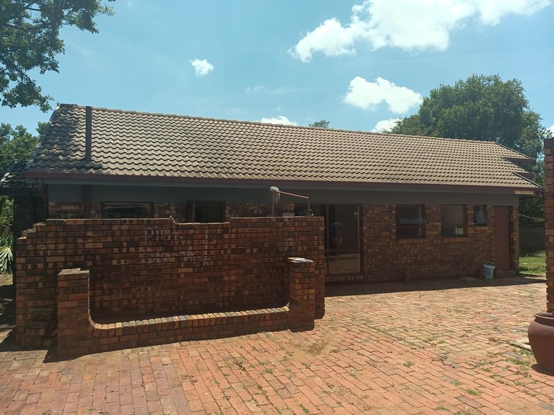Rear view of a face brick house featuring a tiled roof, brick paved patio area, and a low brick boundary wall.