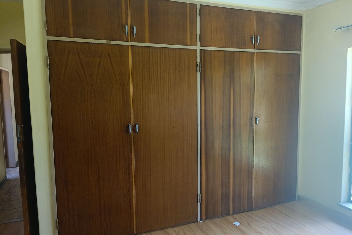 A bedroom featuring dated floor-to-ceiling built-in wooden cupboards and laminate flooring, offering a blank canvas for modernization.