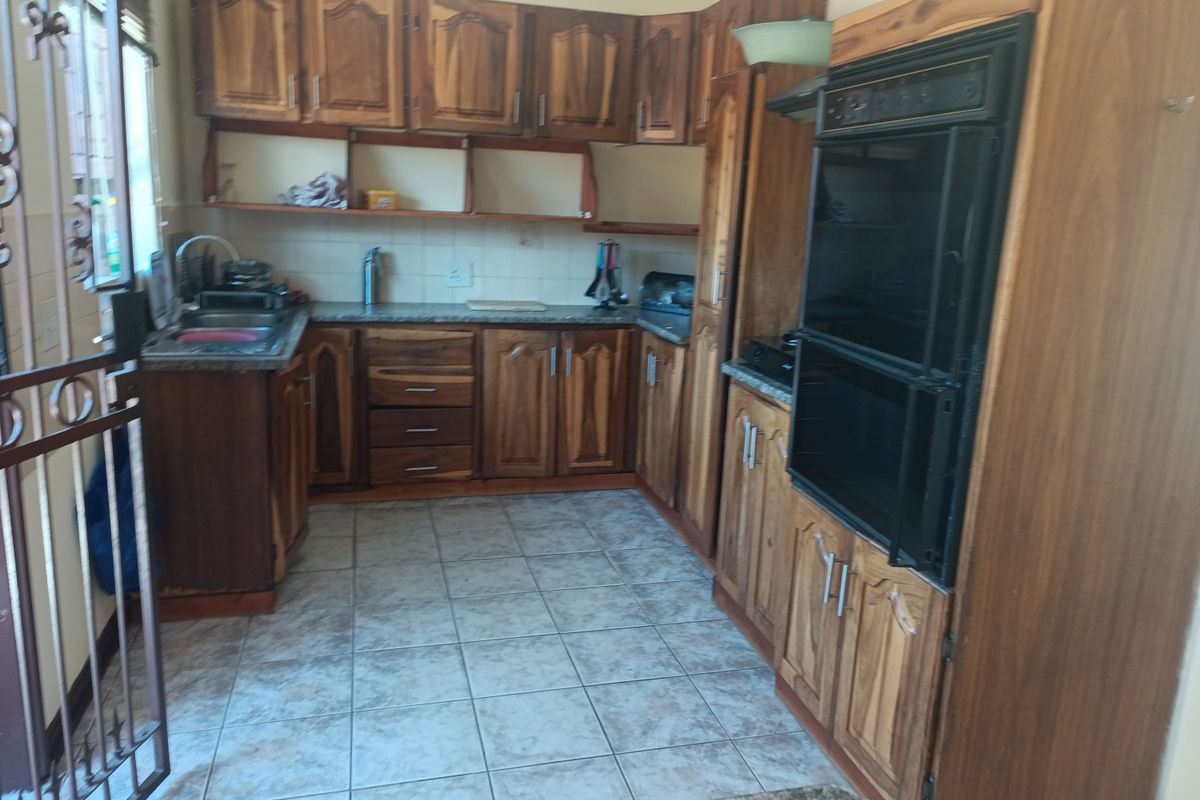 A dated kitchen featuring wooden cabinetry, built-in double oven, laminate countertops, and tiled flooring, offering potential for a modern renovation.