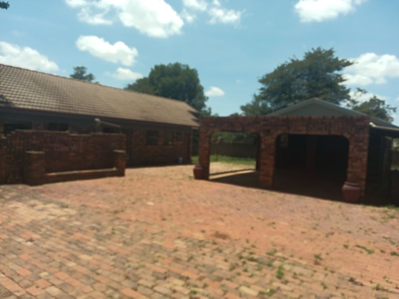Front exterior view of the property featuring a brick facade, tiled roof, and a covered carport area with brick paving.